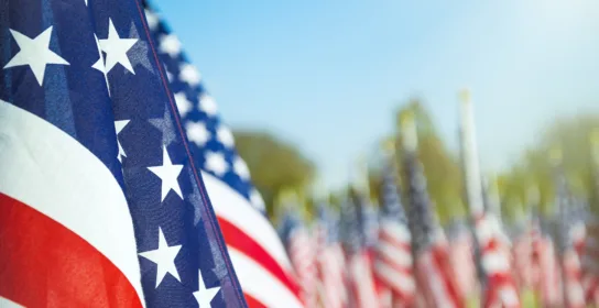 Close-up of an American flag in the foreground, with multiple American flags blurred in the background on a sunny day—representing the aspirations of those seeking guidance from a Chicago EB-3 visa lawyer.