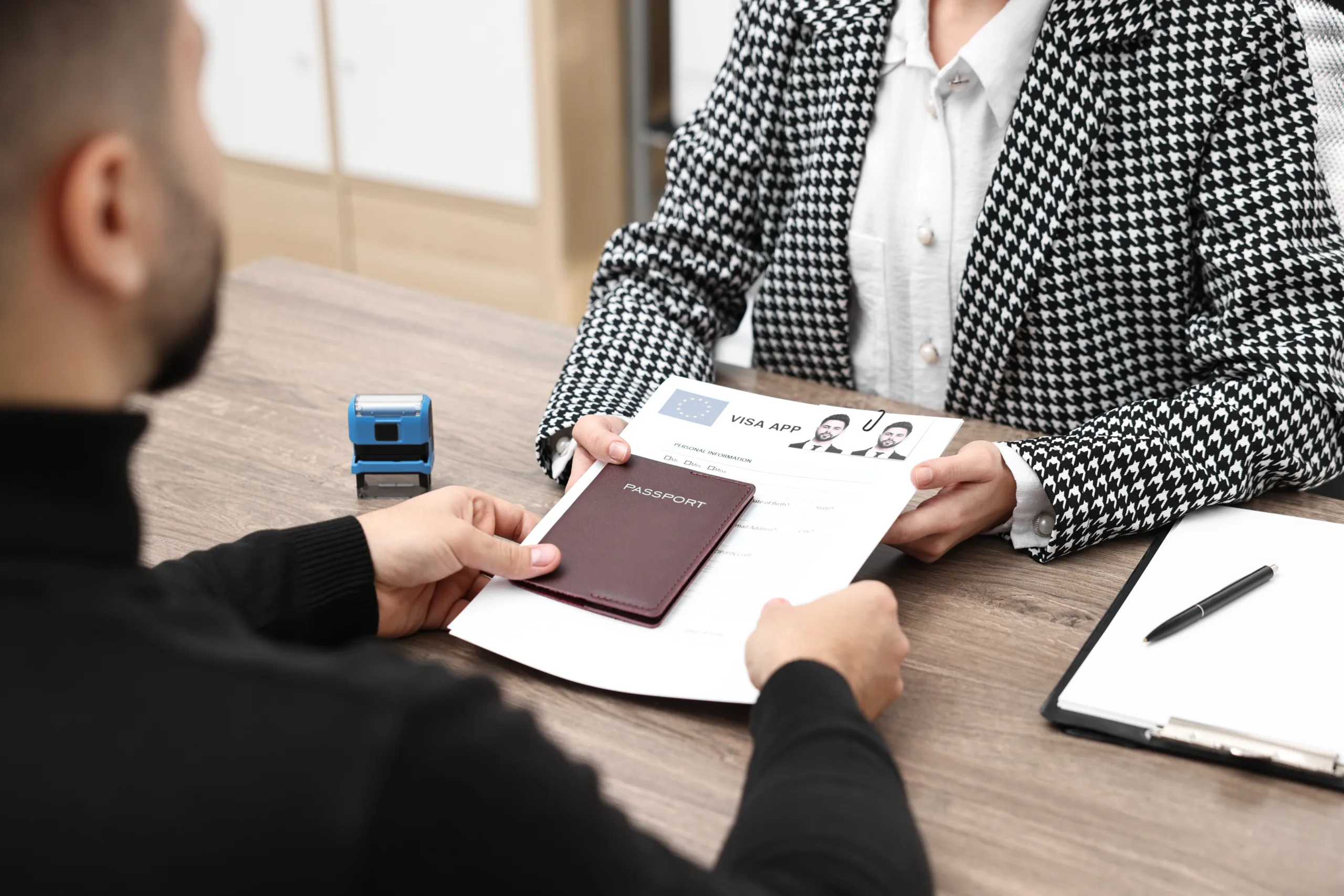 Person hands over a passport and visa application form to an official sitting at a desk with a stamp and clipboard, seeking guidance from an experienced employment visa lawyer in Chicago.